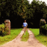 a man is walking down a dirt road in a field