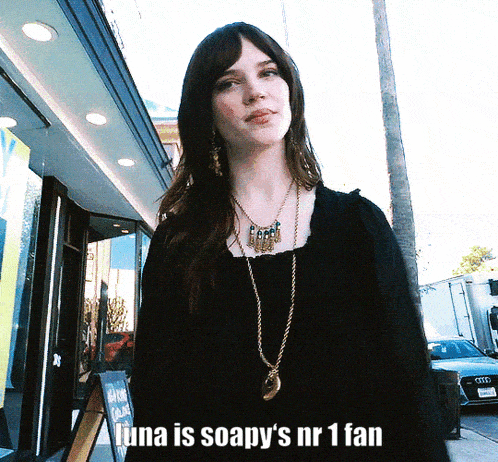 a woman wearing a black top and a gold necklace stands in front of a sign that says luna