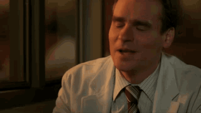a close up of a man in a white coat and tie with his mouth open
