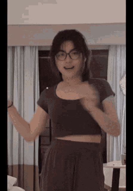 a young woman wearing glasses and a crop top is dancing in a room .