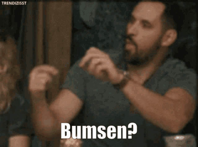 a man with a beard is making a heart shape with his hands and the word bumsen is on the bottom