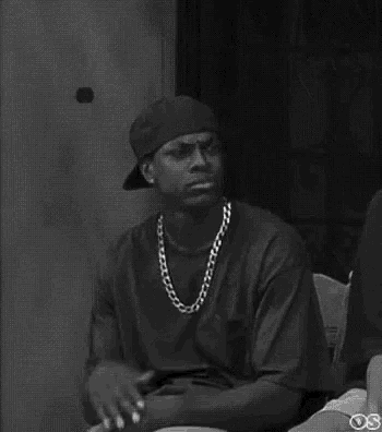 a black and white photo of a man wearing a hat , necklace , and ring .