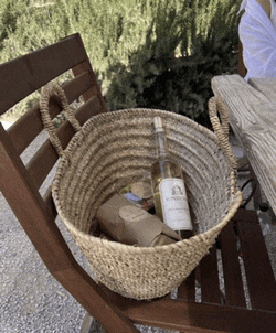 a bottle of wine is in a basket on a wooden chair