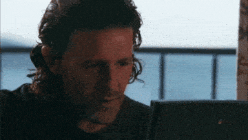 a man with long hair and a beard is looking at a laptop screen