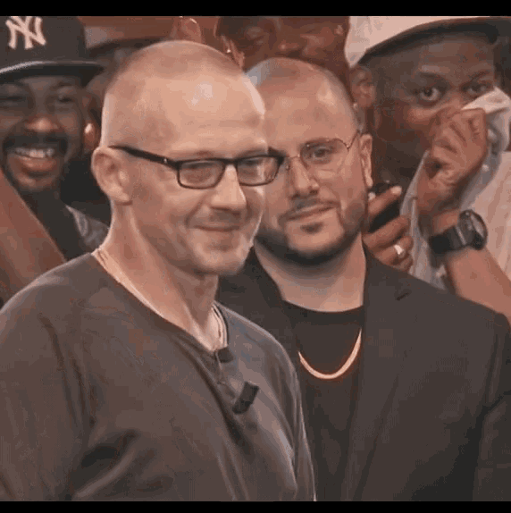 a man wearing glasses and a ny hat smiles in a crowd of people