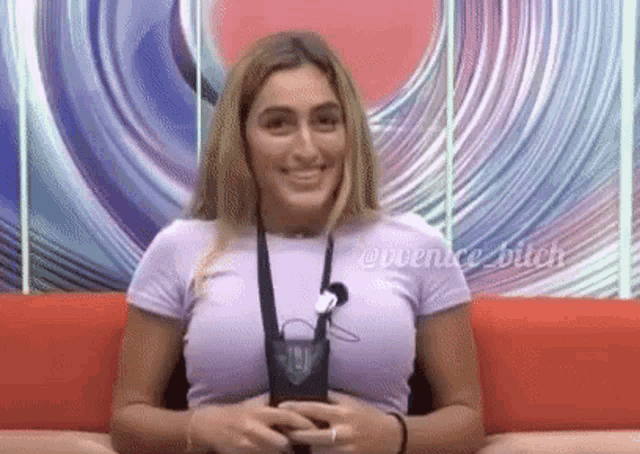 a woman in a purple shirt is sitting on a red couch with a microphone around her neck .