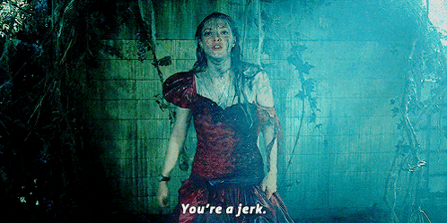 a woman in a red dress is standing in a dark room and says `` you 're a jerk . ''