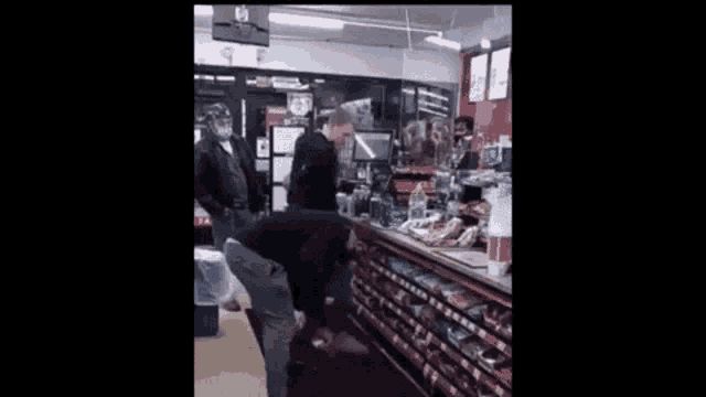 a man is kneeling down in front of a counter at a convenience store .