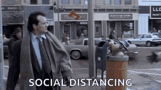 a man in a suit and tie is walking down a city street next to a trash can and a mailbox .
