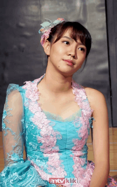 a woman in a blue and pink dress is sitting in front of a sign that says antv kliki