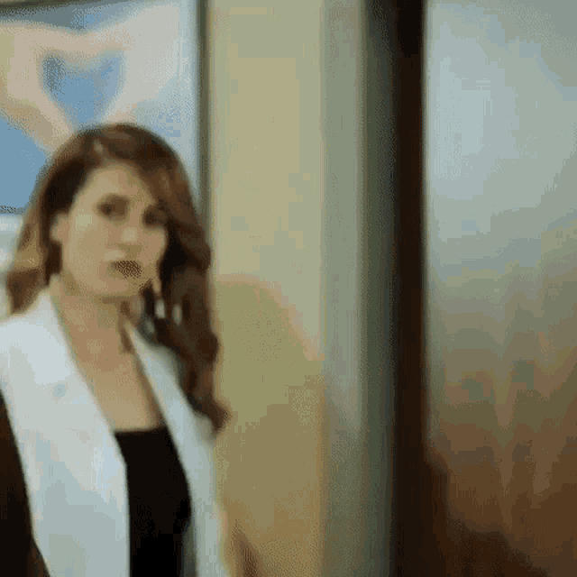 a woman in a white jacket is standing in front of a door and making a heart shape with her hands .