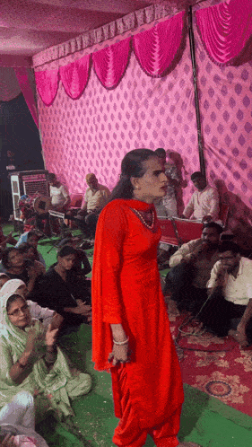 a woman in a red dress stands in front of a pink curtain
