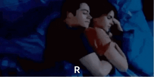 a man and a woman are sleeping next to each other on a bed with the letter r above them .