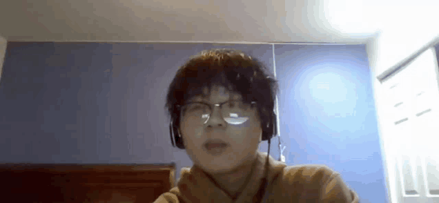 a man wearing glasses and headphones is sitting in front of a blue wall .