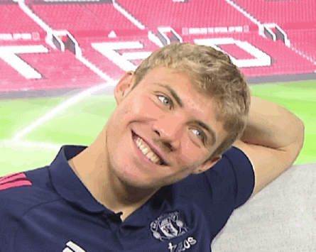 a young man wearing a blue adidas shirt smiles with his hand behind his head