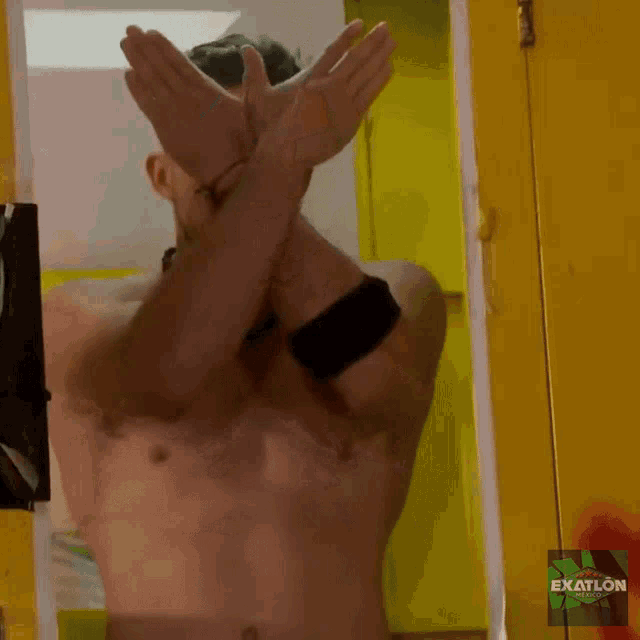 a man without a shirt is standing in front of a yellow door that says exatlon