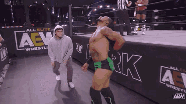 a man in a hoodie is standing next to a wrestler in a wrestling ring that says aew
