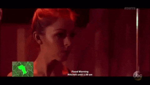 a woman with red hair is standing in a dark room with a flood warning .