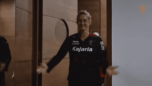 a woman wearing a kajaria jersey is standing in a hallway
