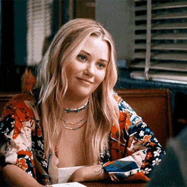 a woman with blonde hair is sitting at a table in front of a window
