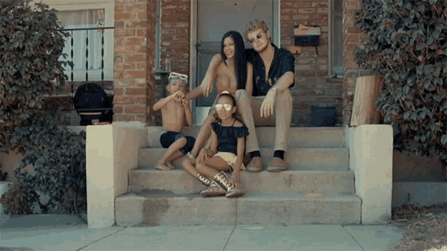 a family sits on the front steps of a house with a mailbox in the background