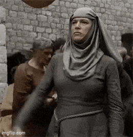 a woman in a gray dress and hijab is standing in front of a brick wall .
