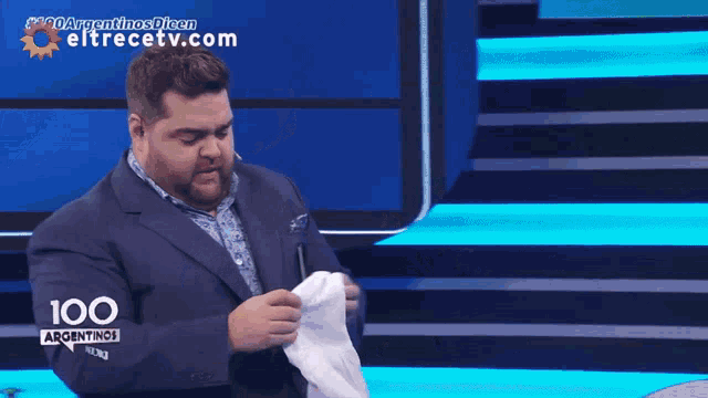 a man in a suit is holding a white shirt in front of a screen that says argentinas