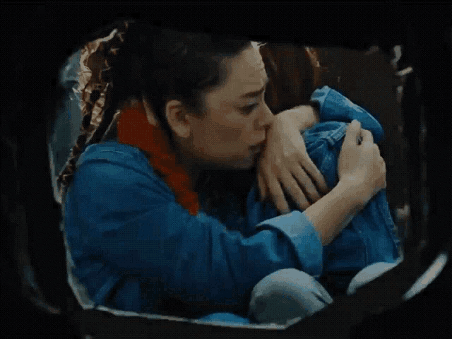 a woman in a blue denim jacket is hugging her knees