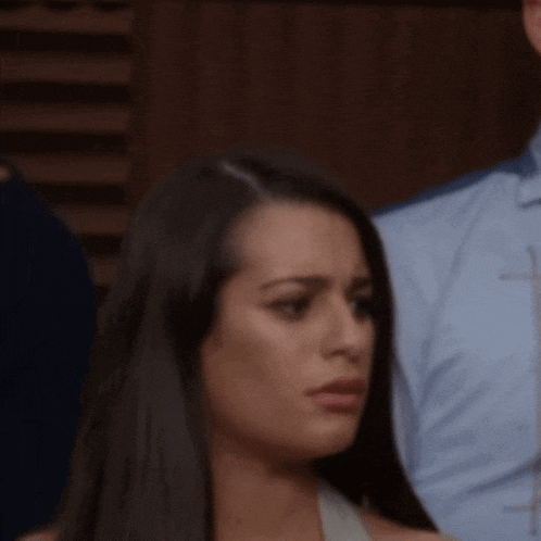 a close up of a woman 's face with a man in a blue shirt in the background