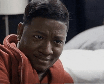 a man in a red hoodie is making a funny face while sitting on a bed .