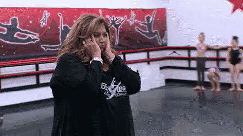 a woman covering her ears in a dance studio with a dance company logo on her shirt