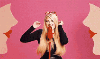 a woman is singing into a red microphone with a pink background behind her .