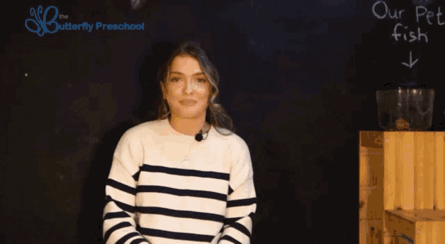 a woman in a striped sweater says perfect in front of a blackboard that says our pet fish
