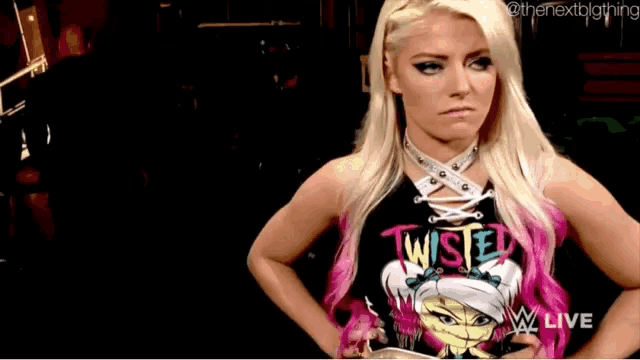 a blonde woman wearing a twisted shirt is standing with her hands on her hips .