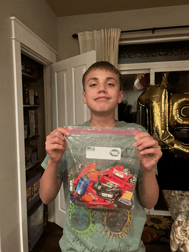 a boy is holding a bag of candy including snickers