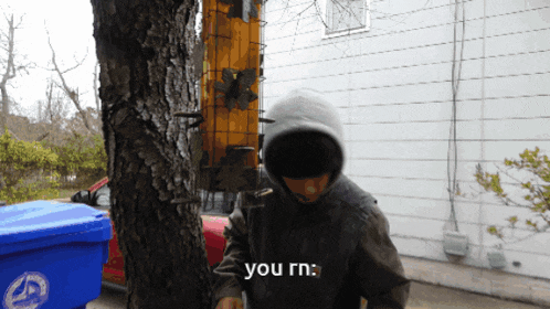 a person in a hooded jacket is standing next to a tree with the words you rn below them