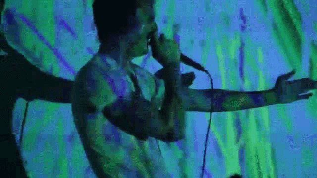 a man singing into a microphone with a green and blue background