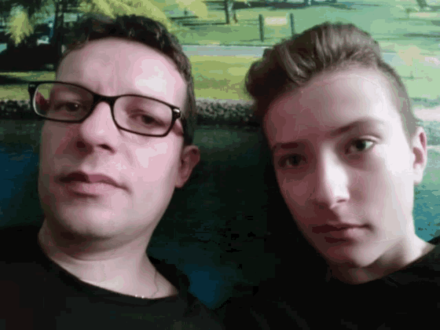 a man wearing glasses and a boy wearing a black shirt pose for a picture