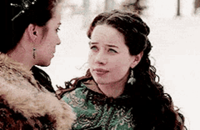 two women are standing in the snow looking at each other .