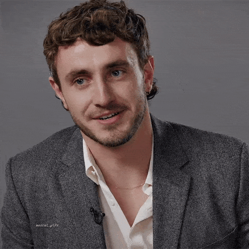 a man with curly hair and a beard is wearing a gray suit jacket and white shirt .