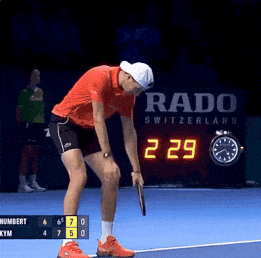 a tennis player holds a racket in front of a rado switzerland sign
