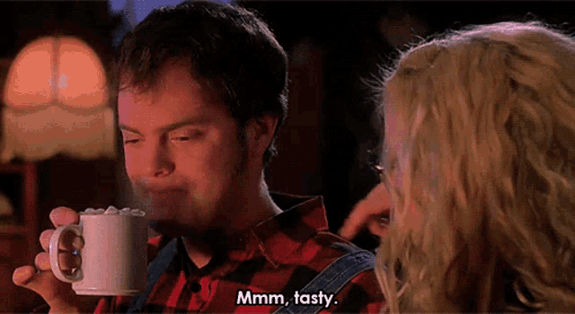 a man in a plaid shirt is drinking from a white mug while a woman says " mmmm tasty "