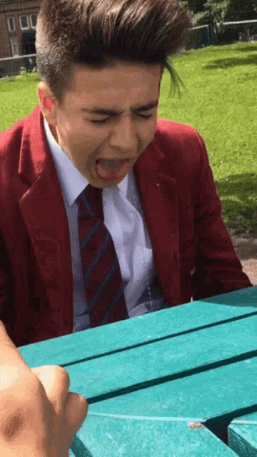 a boy in a red jacket and tie is sitting at a blue table