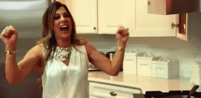 a woman is standing in a kitchen with her arms in the air and laughing .
