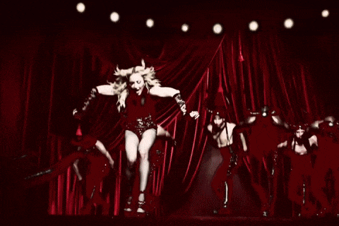 a group of people are dancing on a stage with a red curtain in the background
