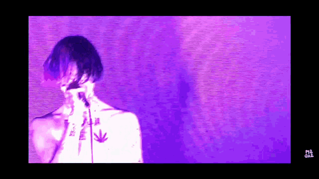 a man with a marijuana leaf tattoo on his chest sings into a microphone