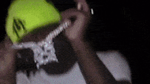 a man wearing a yellow hat and a necklace with diamonds on it is playing a guitar .