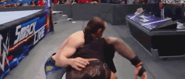 two men are wrestling in a wrestling ring and one of them is hugging the other .
