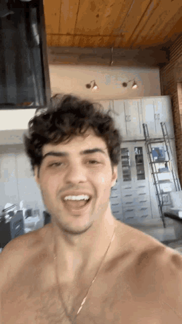 a shirtless man is smiling in a kitchen with a ladder