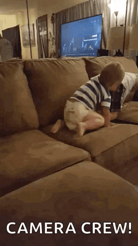 a little boy is crawling on a couch with the words camera crew behind him .